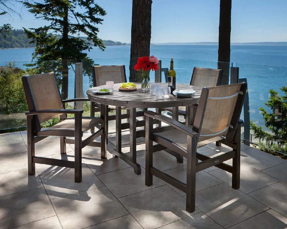 Outdoor dining set with sling chairs and a round table overlooking a waterfront view, ideal for resorts and luxury properties.
